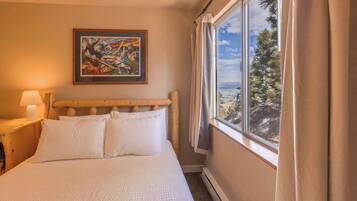 A bedroom with a bed, a nightstand, a lamp, a painting, and a window with curtains.