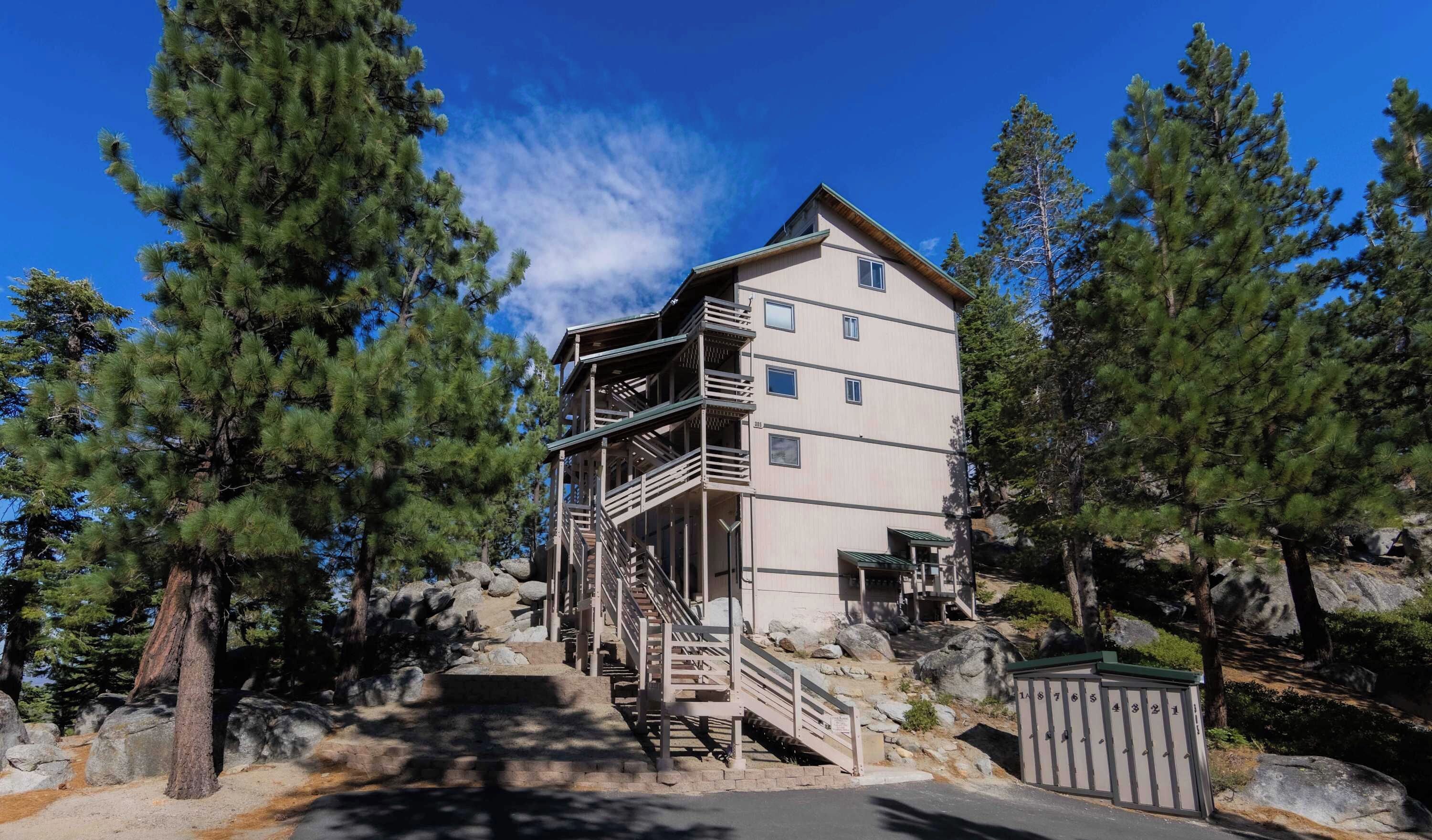 A multi-story building with a staircase leading to an upper level, surrounded by trees and rocks.