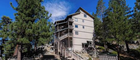 A multi-story building with a staircase leading to an upper level, surrounded by trees and rocks.