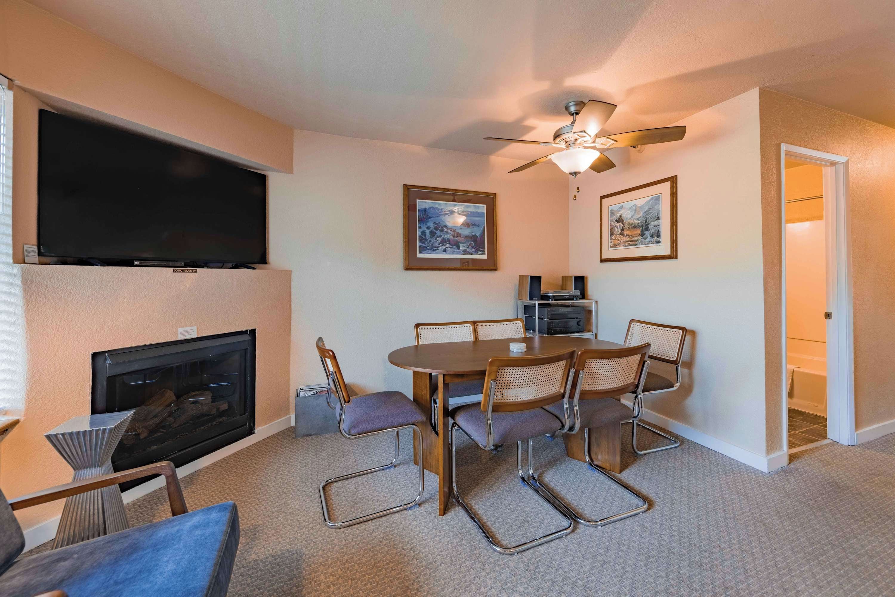 A living room with a flat-screen TV, fireplace, dining table with chairs, ceiling fan, and two framed pictures on the wall.