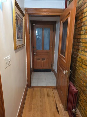 A hallway with a wooden door, a radiator, and a tiled floor. - Charming 1-bedroom apartment with AC in vibrant Brooklyn (Brooklyn)
