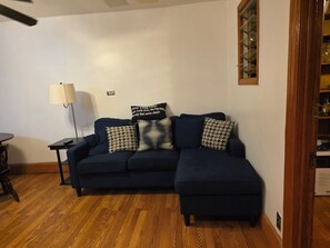 A living room with a dark blue sectional sofa, a lamp, and patterned cushions. - Charming 1-bedroom apartment with AC in vibrant Brooklyn (Brooklyn)