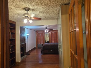 A hallway with a ceiling fan, a brick wall, a radiator, and a bed in the distance. - Charming 1-bedroom apartment with AC in vibrant Brooklyn (Brooklyn)