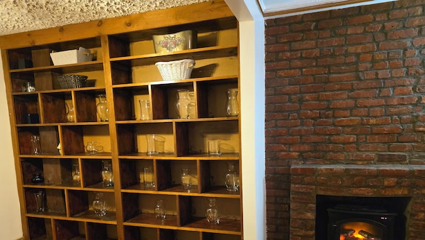 Ein Zimmer mit Holzboden, einem Kamin aus Ziegelsteinen und einer Regalanlage mit unterschiedlichem Glas und Körben.