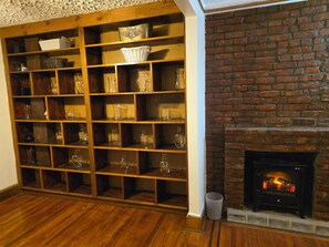 A room with a wooden floor, a brick fireplace, and a shelving unit with various glassware and baskets. - Charming 1-bedroom apartment with AC in vibrant Brooklyn (Brooklyn)