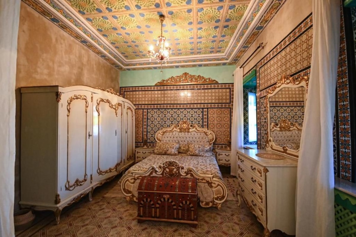 Ein Zimmer mit einem großen Bett, einem verzierten Kopfteil und einer gemusterten Decke.