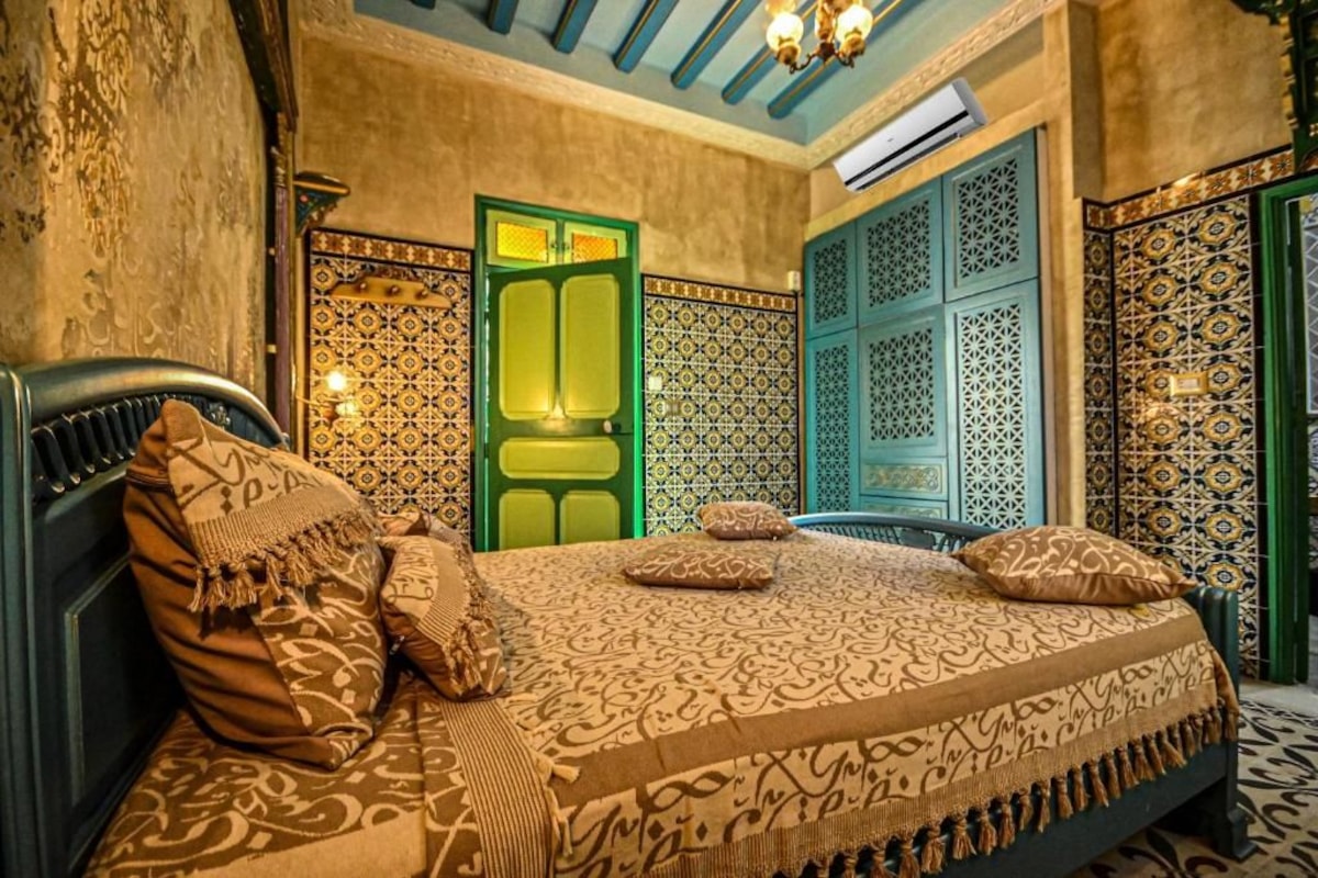 Ein Zimmer mit einem Bett, gemusterten Wänden und einer grünen Tür.