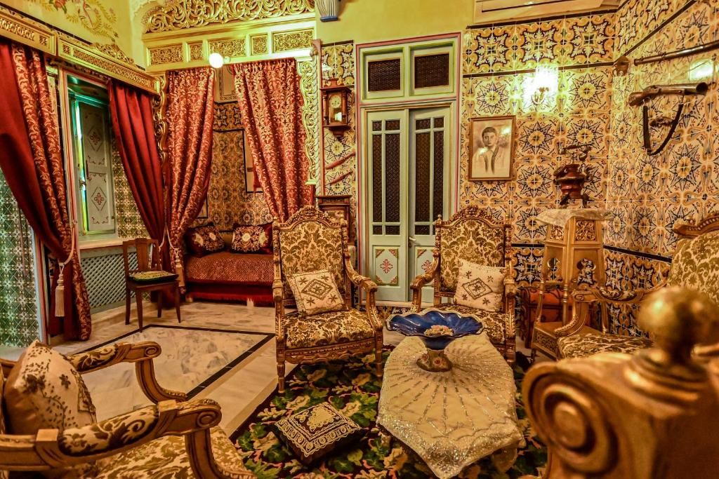 An ornate room with traditional furnishings, including a sofa, chairs, and a bed with intricate designs.
