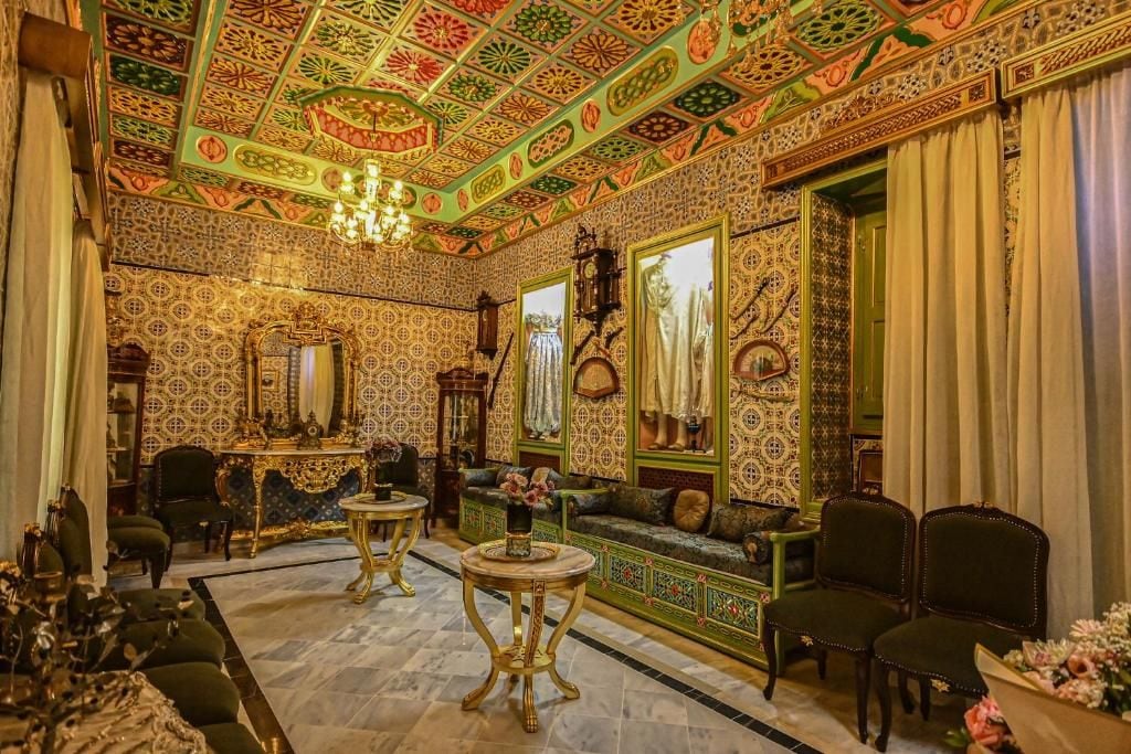 Una habitación con papel tapiz decorativo, un candelabro y muebles tradicionales.