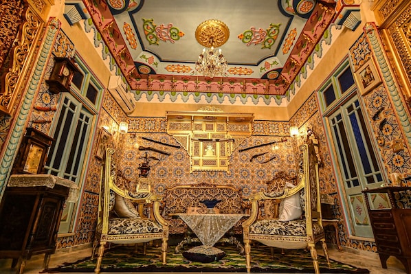 An ornate room with intricate tile work, a chandelier, and a central table with two chairs.
