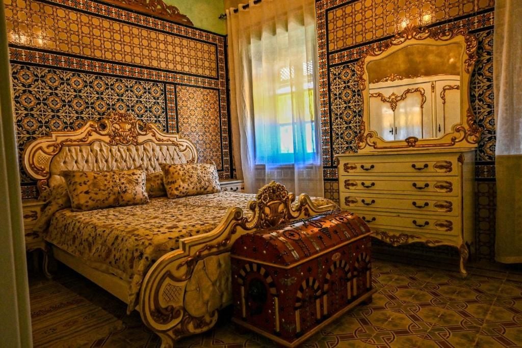Ein Schlafzimmer mit einem großen Bett, einem verzierten Schmuckkästchen und Wandmustern.