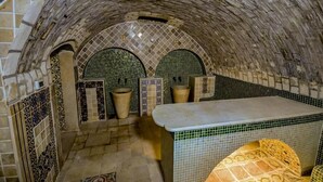 A stone-walled room with a tiled floor, a bench, and a tiled wall with a decorative pattern. - Dar Koraich (Kairouan)