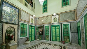 A courtyard with a checkered floor, green doors, and patterned tiles. - Dar Koraich (Kairouan)