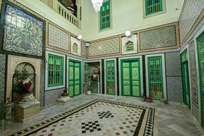 Ein Innenhof mit Schachbrettboden, grünen Türen und gemusterten Fliesen.