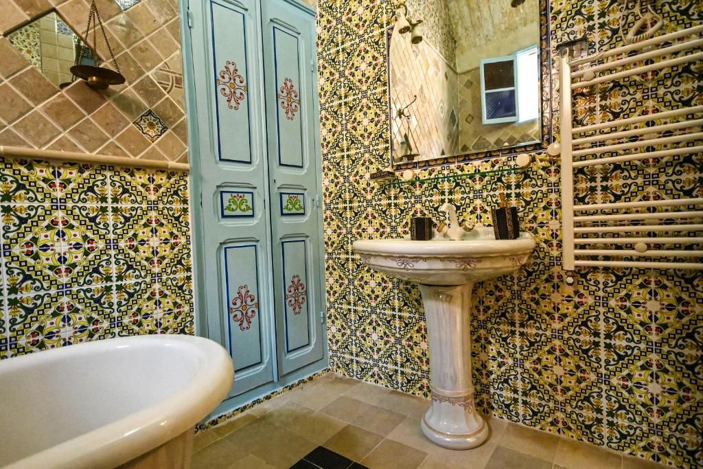 A bathroom with a bathtub, a pedestal sink, and a tiled wall with a geometric pattern.