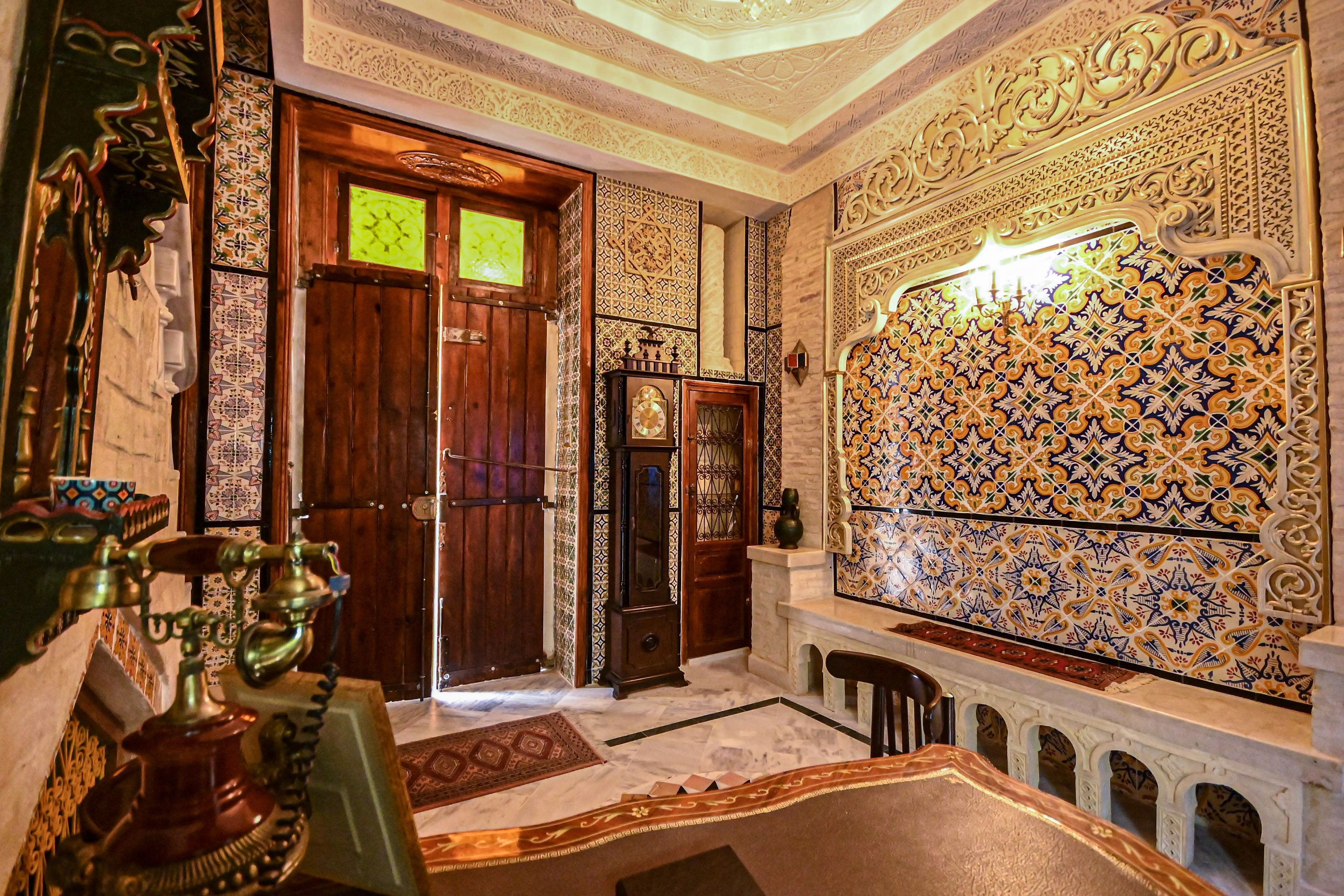 An ornate room with intricate tile work, a wooden door, and a traditional water fountain.