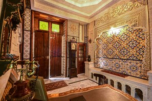 An ornate room with intricate tile work, a wooden door, and a traditional water fountain. - Dar Koraich (Kairouan)