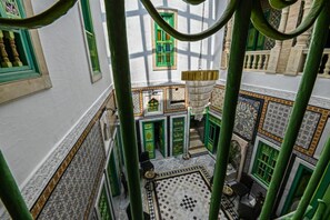 Un patio con una fuente central, rodeado de ventanas con marcos verdes y baldosas de suelo con diseños.