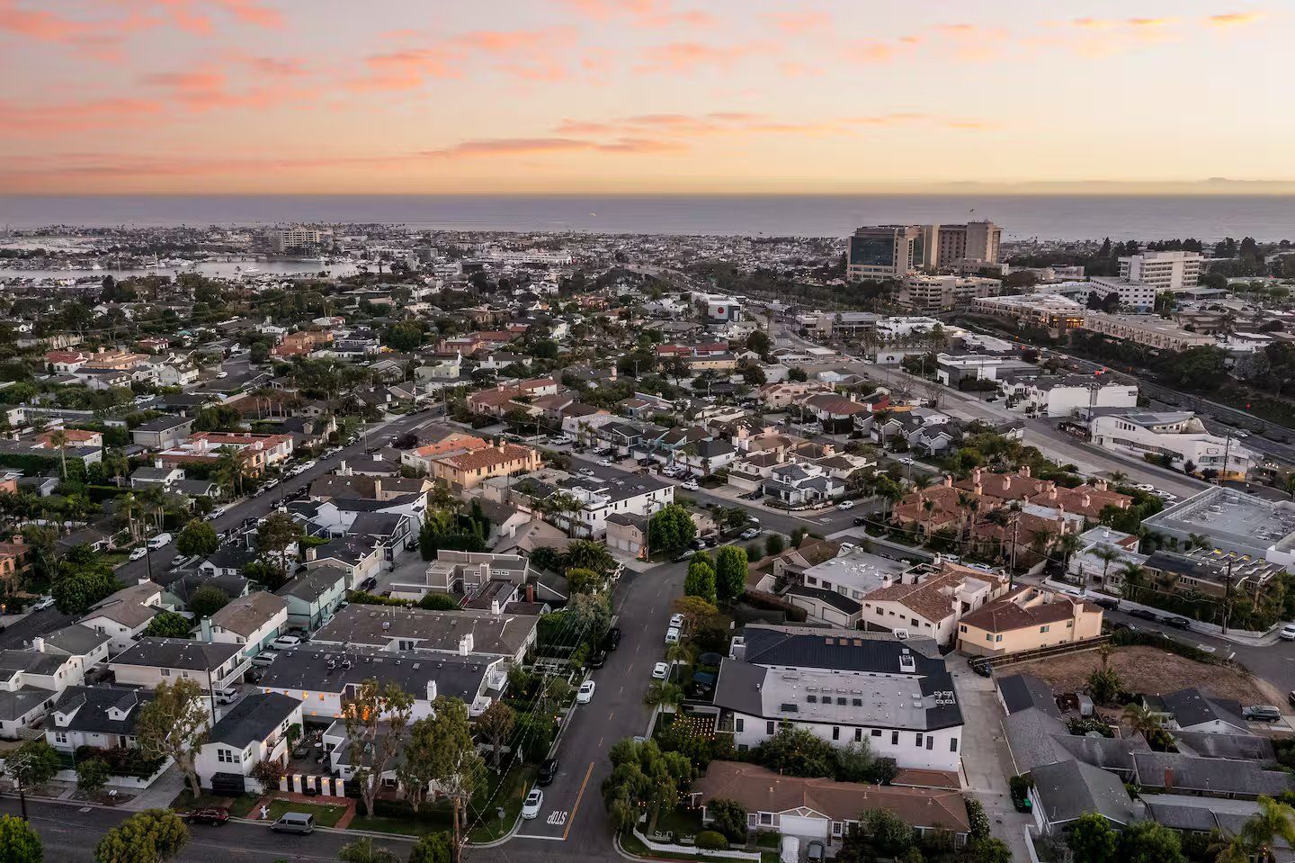 A residential area with a mix of single-family homes and apartment buildings, roads, and a distant view of the ocean.