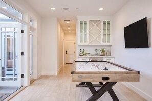 A modern kitchen with a wooden table, white cabinets, and a TV mounted on the wall. - Stunning Home, Mins to Beach, Perfect for Families W/AC! (Newport Beach)