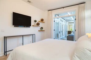Ein Hotelzimmer mit Bett, Fernseher, Schreibtisch und Blick auf den Hotelkorridor.