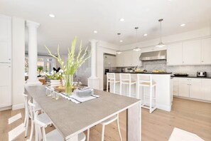 A modern kitchen with white cabinetry, a wooden dining table, and pendant lighting. - Mins To Newport Beach, Pier, Water-Front Dining (Newport Beach)