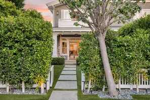 Ein zweistöckiges Haus mit einer Veranda, einem Weg zum Eingang und einem großen Baum in der Mitte.
