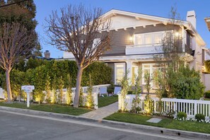 Une maison à deux étages avec un porche à l’avant, une boîte aux lettres et une clôture blanche faite de piquets.