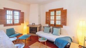 A cozy living room with a fireplace, a sofa with cushions, a chair, a small table, and a lamp. - La Casita Sayalonga by Ruralidays (Málaga)