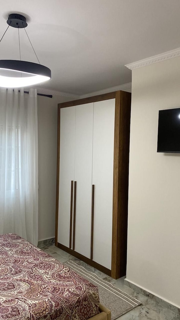 Un dormitorio con una cama, un armario, un televisor y una lámpara colgante.
