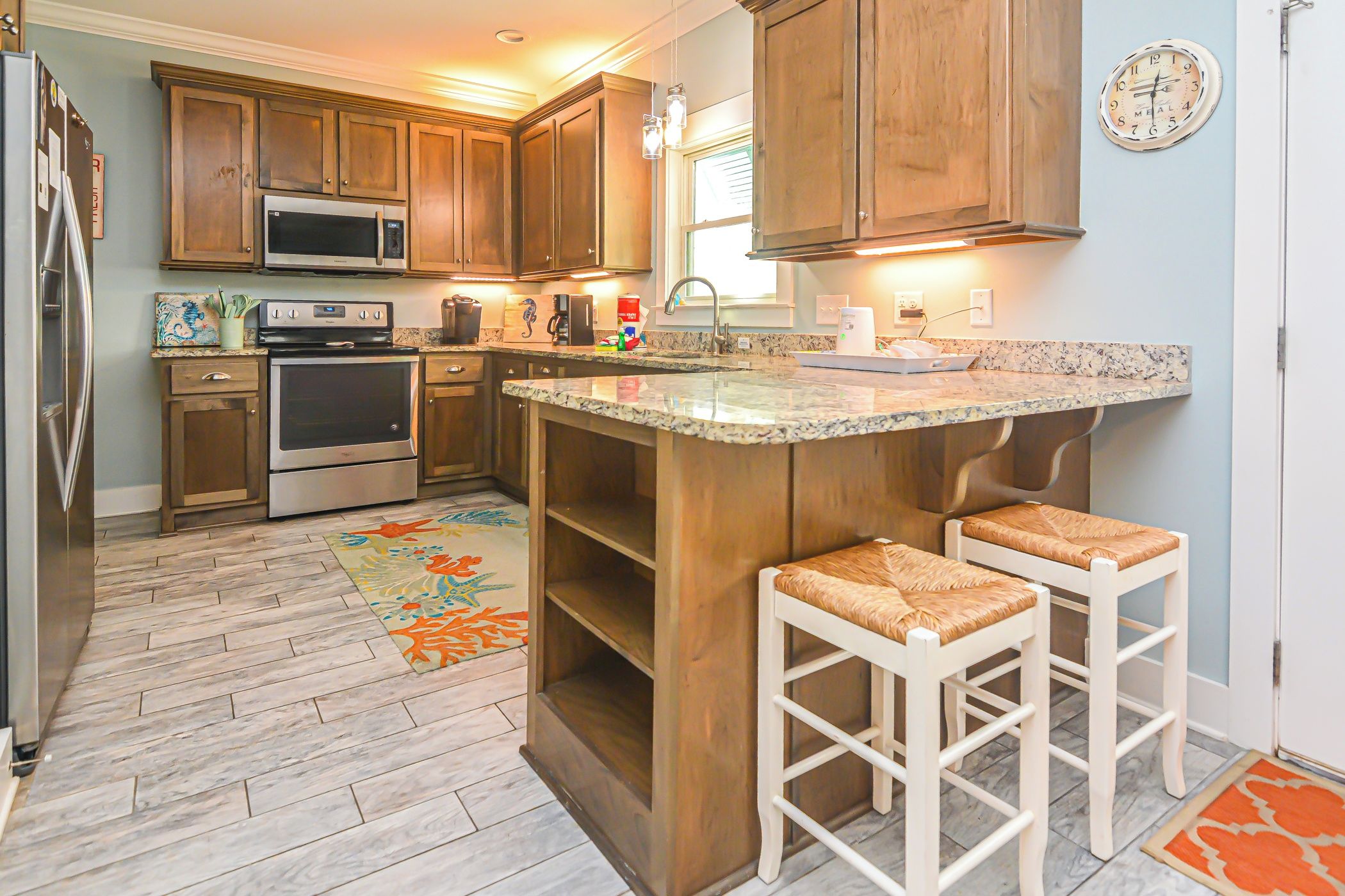 A kitchen with wooden cabinets, stainless steel appliances, a granite countertop, and two bar stools.