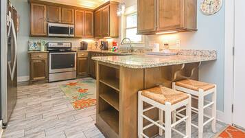 A kitchen with wooden cabinets, stainless steel appliances, a granite countertop, and two bar stools.