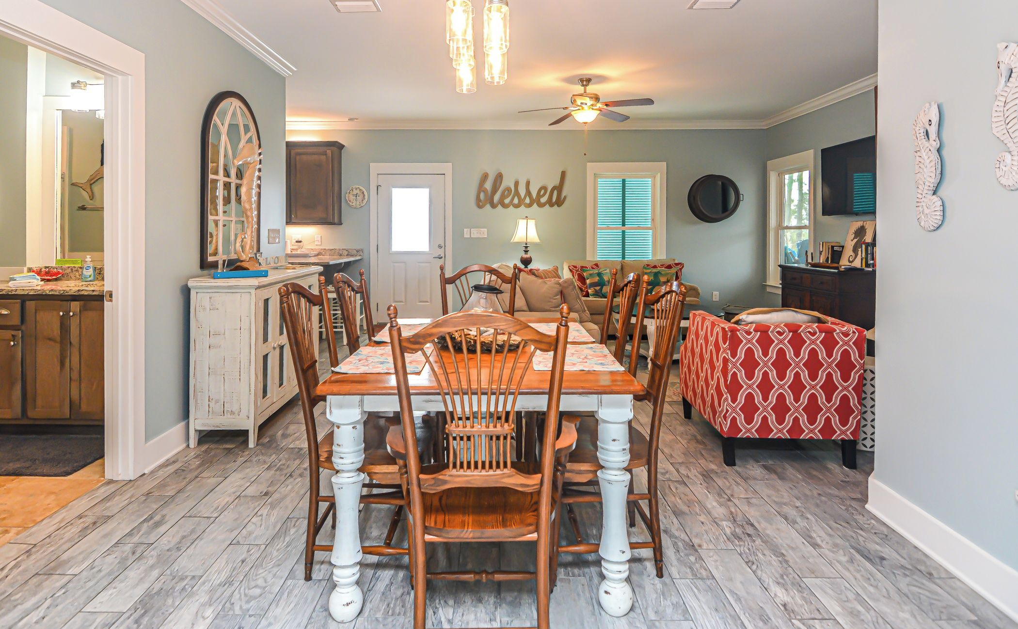 A dining area with a wooden table and chairs, a ceiling fan, and a kitchen in the background.