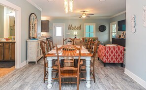 A dining area with a wooden table and chairs, a ceiling fan, and a kitchen in the background. - 6007 Rookery 3 Just Breathe Sea Horse Cottage (Gulf Shores)