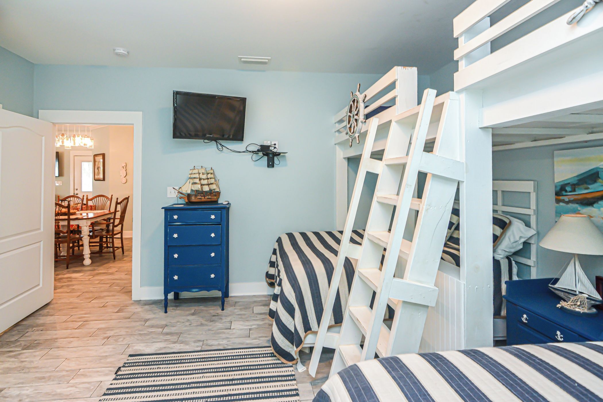 A bedroom with a bunk bed, a desk with a chair, a dresser, and a television on the wall.