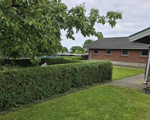 A residential area with a well-maintained lawn, a hedge, and a brick building with a tiled roof. - Bright holiday home near beach and coast (Hejls)