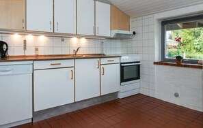 A kitchen with white cabinets, a stove, and a window with a view of greenery. - Bright holiday home near beach and coast (Hejls)