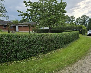 A well-maintained hedge, a grassy lawn, and a brick building with a garage. - Bright holiday home near beach and coast (Hejls)