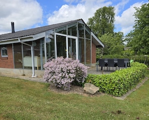 A brick building with large windows and a glass extension, surrounded by a well-maintained lawn and flowering bushes. - Bright holiday home near beach and coast (Hejls)