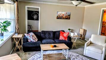 A living room with a sofa, a coffee table, a chair, a ceiling fan, and a painting on the wall.