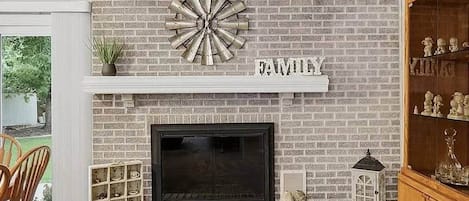 A fireplace with a brick wall, a shelf above it, and a word 'FAMILY' on the wall.