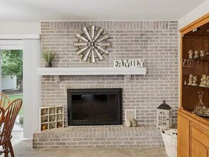 A fireplace with a brick wall, a shelf above it, and a word 'FAMILY' on the wall. - Poolside Pokes (Stillwater)