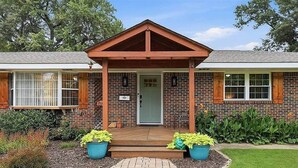 A two-story brick building with a covered porch, a front door, and a small garden area with potted plants. - Poolside Pokes...Walk to OSU!!! (Stillwater)