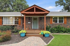 A two-story brick building with a covered porch, a front door, and a small garden area with potted plants. - Poolside Pokes...Walk to OSU!!! (Stillwater)