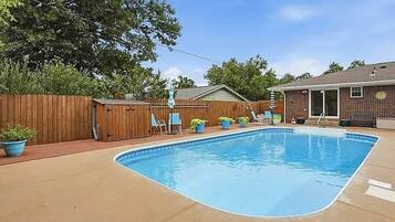 A backyard with a swimming pool, wooden fence, and outdoor furniture.