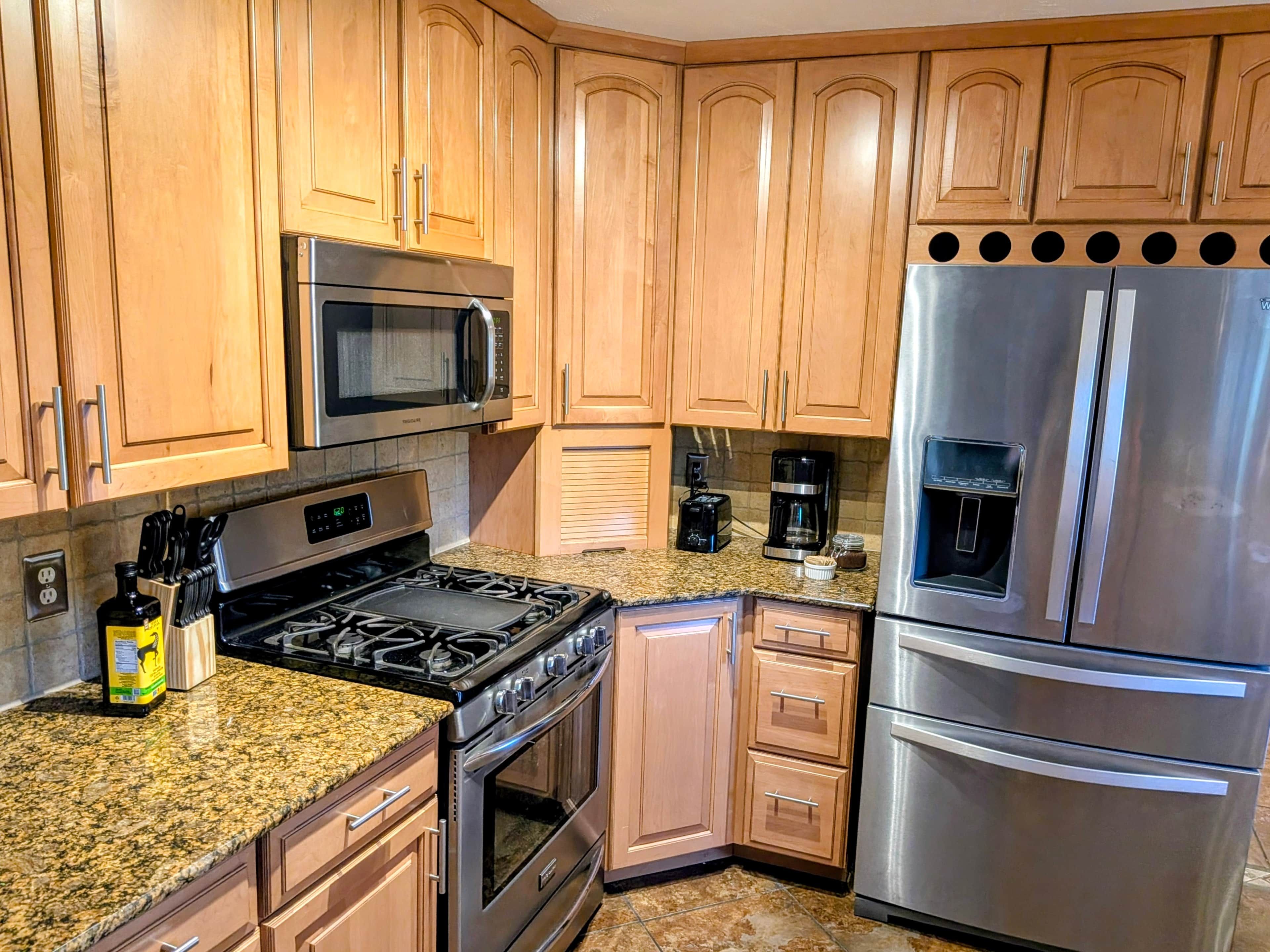 A kitchen with wooden cabinets, stainless steel appliances including a microwave, stove, and refrigerator, and granite countertops.