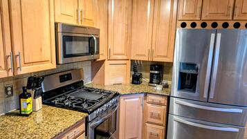 A kitchen with wooden cabinets, stainless steel appliances including a microwave, stove, and refrigerator, and granite countertops.