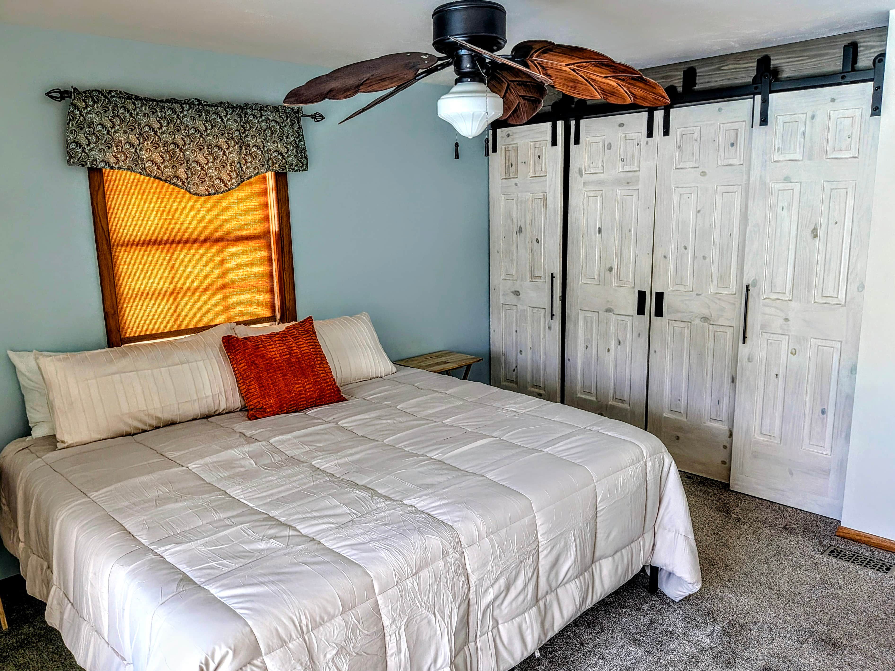 A bedroom with a bed, a ceiling fan, a window with a curtain, and a wardrobe.
