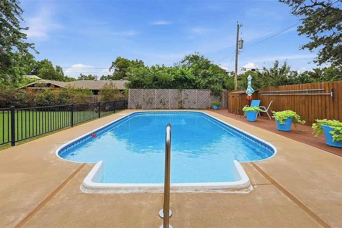 A rectangular swimming pool with a metal ladder in the center, surrounded by a wooden fence and potted plants.