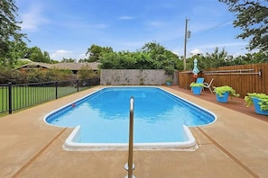 A rectangular swimming pool with a metal ladder in the center, surrounded by a wooden fence and potted plants.